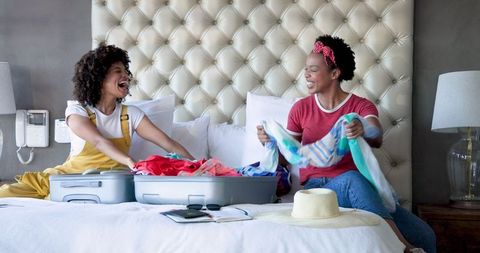 Joyful Diverse Female Couple Packing Suitcase for Vacation