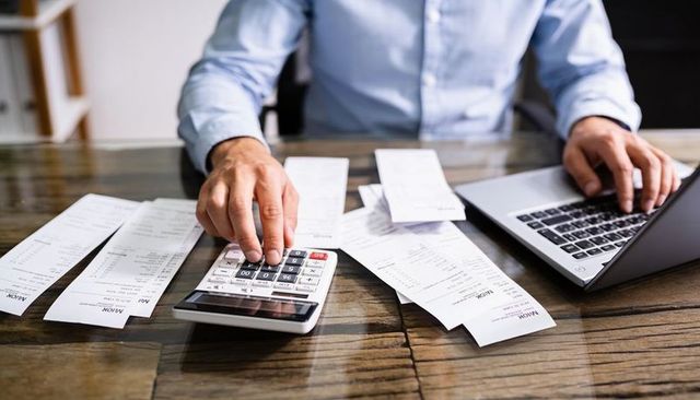 Calculating receipts and balancing budget with laptop and calculator on wooden desk