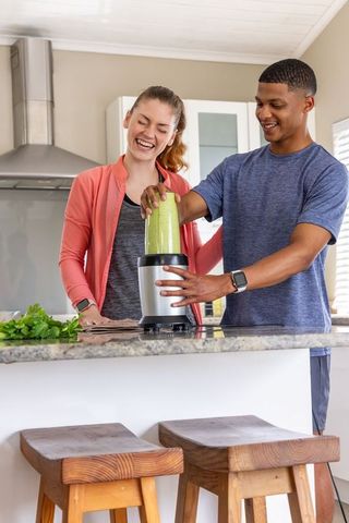 Couple making green smoothie together in modern kitchen using personal blender