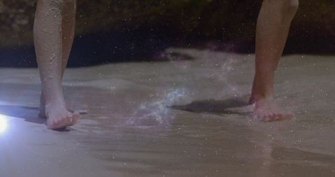 Kids wading barefoot in shallow shoreline water showing footprints and lens flare