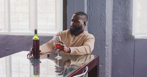 African American Man Relaxing with Wine at Stylish Glass Table