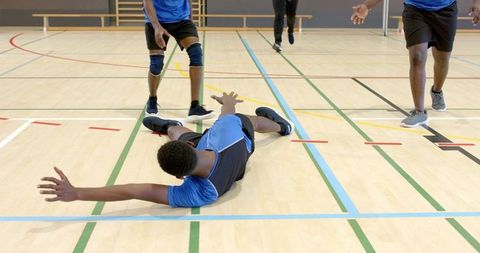 Diverse male team reaching and recovering on hardwood court during intense indoor training