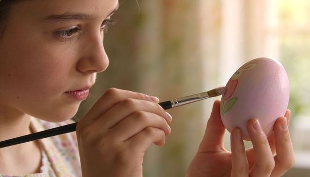 Young girl painting pastel easter egg with soft focused expression and delicate brushwork
