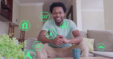 Smiling man sitting on sofa using smart home energy app with eco icons in living room