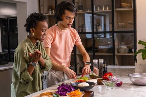 Diverse couple cooking together on marble countertop preparing fresh vegetable bowls