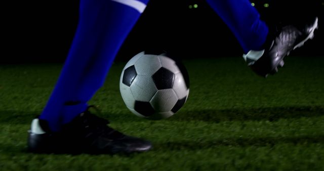 A soccer player in blue sportswear is about to kick a football during a night game, with copy space. Capturing the dynamic movement, this image conveys the intensity and action of a soccer match.
