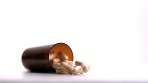 Capsules Spilling from Medicine Bottle on White Background