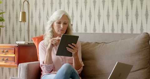 Mature Woman Using Tablet for Work on Sofa in Comfortable Living Room