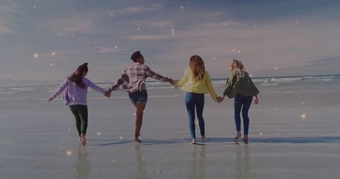 Joyful friends walking on scenic ocean shore at sunset