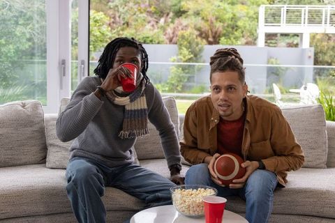 Multicultural friends watching football on couch holding football drinking from red cups