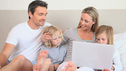 Happy Family Enjoying Time Using Laptop Together in Cozy Bedroom