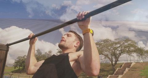 Fit man performing pull-up on bar in outdoor park setting