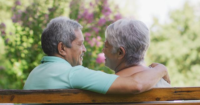Senior couple enjoying a relaxing moment on a park bench, embracing and smiling. Perfect for illustrating themes of elder care, retirement, eternal love, and the joy of outdoor activities for seniors.