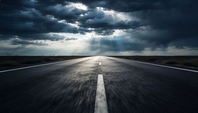 Stretching highway toward dramatic sunbeams through storm clouds over remote plains