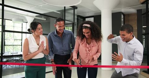 Colleagues cutting red ribbon celebrating office achievement