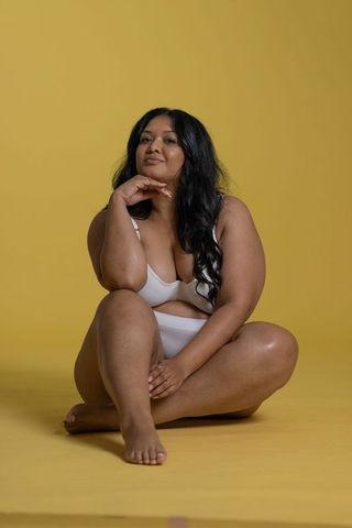 Confident plus-size woman sitting in white lingerie on yellow background