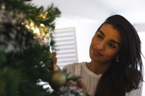 Middle eastern woman decorating beautiful christmas tree indoors