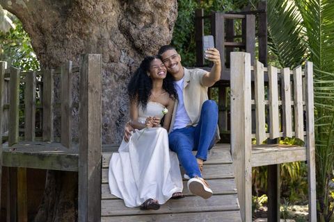 Smiling couple taking romantic selfie on wooden treehouse platform in sunlit park