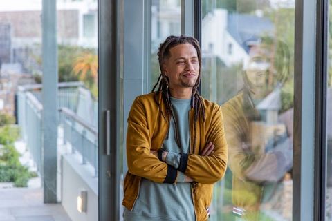 African american man leaning with arms crossed, gazing through glass on balcony