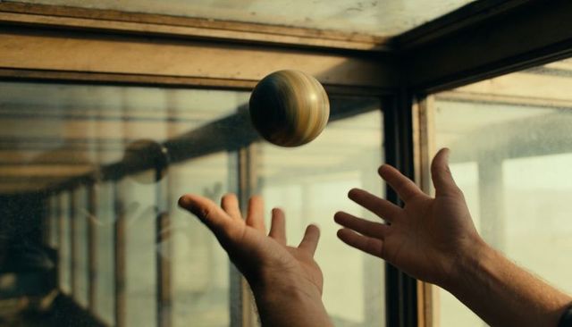 Hands reaching for striped wooden ball in glass corridor with warm desaturated light