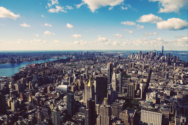 Capturing breathtaking aerial view of New York City with iconic skyline. Skyscrapers standing tall under blue sky with scattered clouds. Image ideal for travel brochures, city guides, urbanization studies, and real estate advertising.