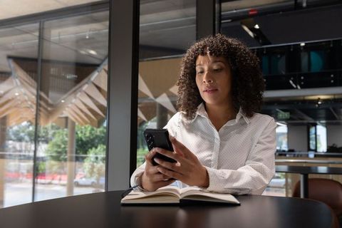 Professional Woman Using Smartphone and Notebook in Modern Cafe