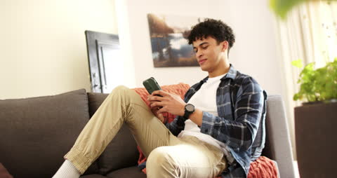 Young Man Relaxing on Sofa with Smartphone at Home