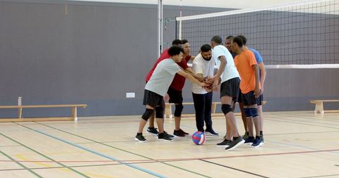 Multiracial male volleyball team huddling and placing hands before match in gymnasium