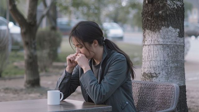 Solitary woman pausing with white mug at streetside cafe table, contemplating outdoors