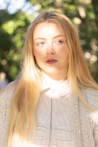 Young blonde woman standing in sunlit park, contemplative outdoor portrait with sunbeam