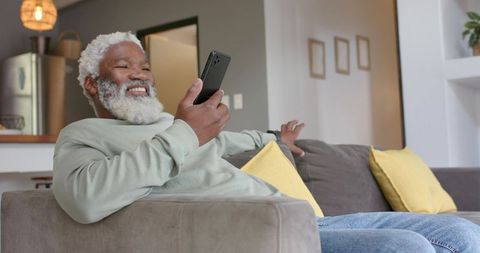 Senior Man Relaxing on Sofa with Smartphone in Modern Home