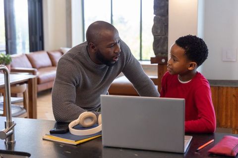 African American Father Helping Son with Homework at Kitchen Island Using Laptop Together