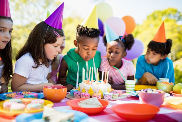 Cute children blowing together on the candle during a birthday party on a park 