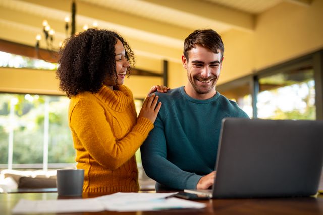 This image depicts a happy couple working together from home, showcasing a modern and flexible work environment. Ideal for use in articles or advertisements about remote work, home office setups, teamwork, and work-life balance.