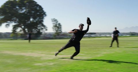 Outfielder diving and reaching for catch while teammates backing up on baseball field