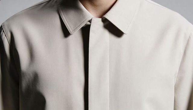 Modeling tailored beige collared coat with concealed placket and refined topstitching