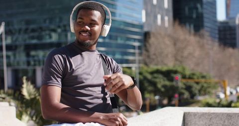 African American man relaxing on urban ledge listening to music with headphones, smartwatch