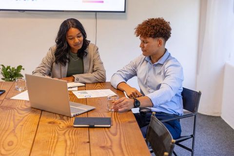 Diverse team reviewing reports and collaborating on strategy around laptop conference table