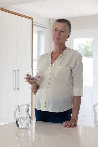 Senior Woman Holding Water Glass in Bright Minimalist Kitchen