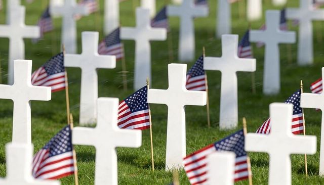 White crosses and american flags honoring fallen soldiers lining military cemetery rows