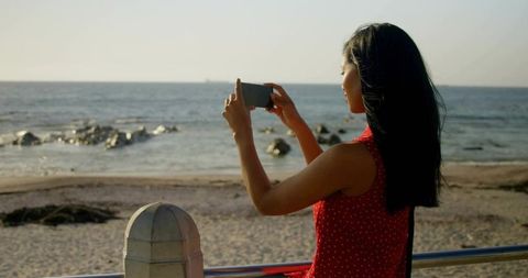 Woman capturing ocean view on smartphone at seaside promenade