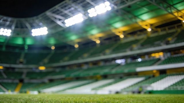 Close-up stadium turf night scene with floodlights, empty green stands and roof trusses