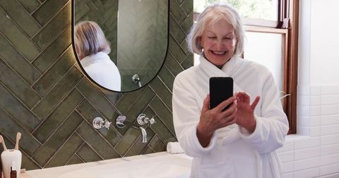 Senior woman enjoying moment with smartphone in modern bathroom