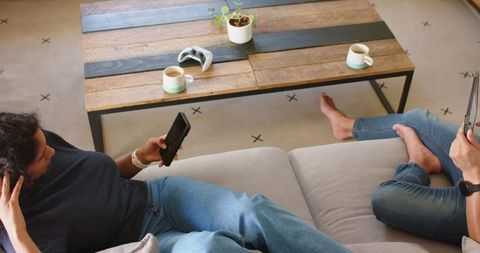 African couple lounging on sofa using smartphones in cozy living room