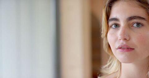 Serene Woman Standing Near Window in Well-Lit Hallway