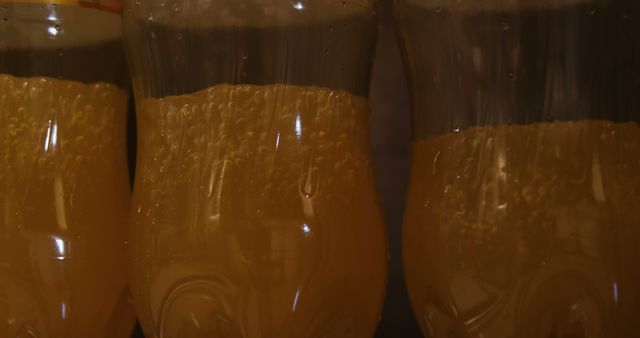 Close-up view of bubbly amber-colored drink in plastic bottles. Bubbles and condensation indicate the beverage is carbonated, making it suitable for visuals related to refreshments, beverages, and drink marketing. Could be used in advertisements, menus, or blogs about summer drinks, carbonated beverages, and refreshment.