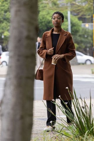 Walking with coffee in brown coat on city sidewalk, urban commuter style, overcast morning