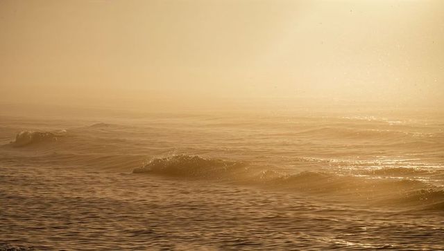 Glinting golden hour ocean surface with gentle breaking waves and hazy horizon