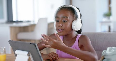 African american teen engaging in remote learning with headphones using tablet at home