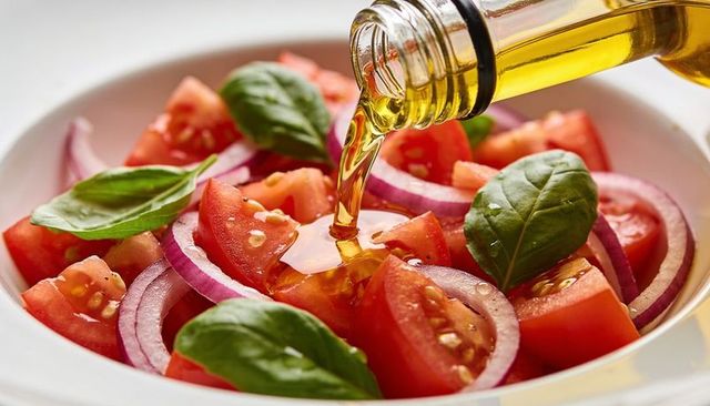 Pouring olive oil over fresh tomato basil salad with red onion — glossy mediterranean